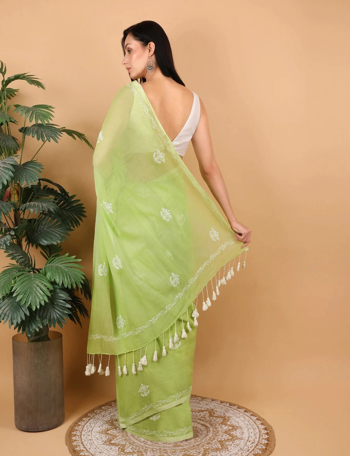 Woman wearing a light green Mulmul saree with white patterns and tassels on a beige background
