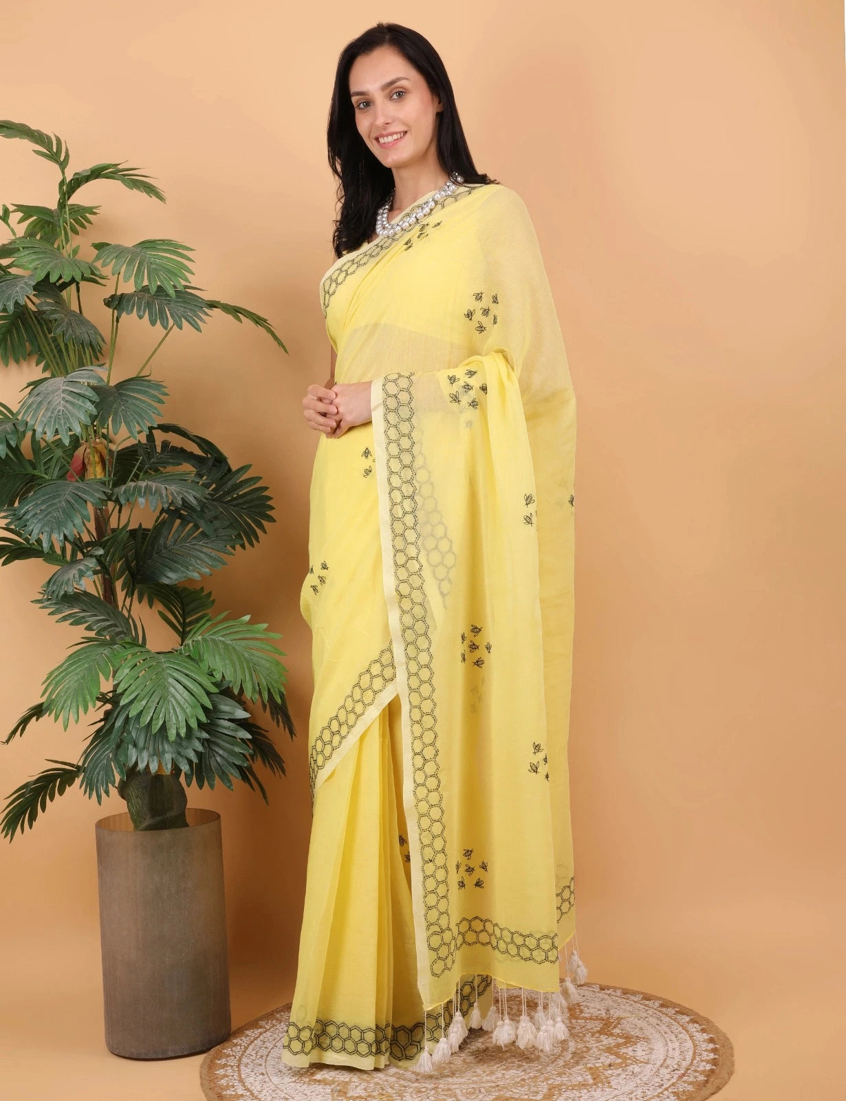 Woman in a yellow Mulmul saree with a plant on a beige background