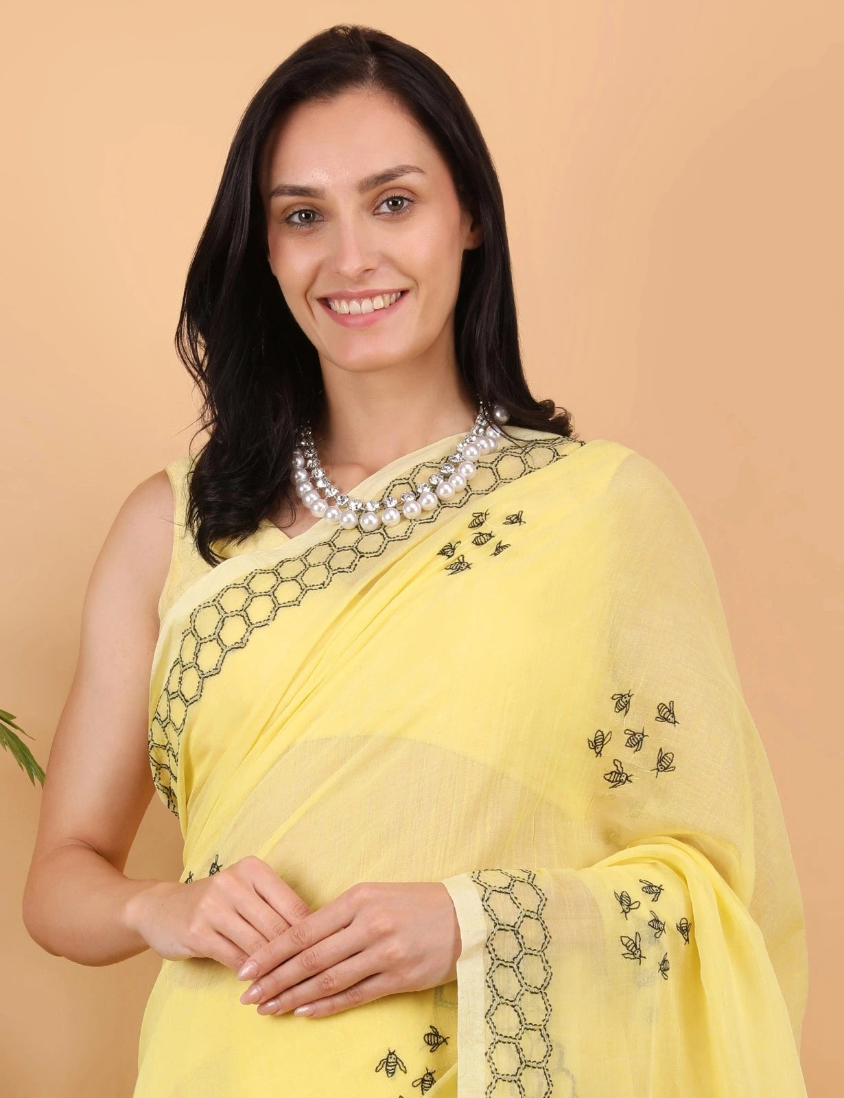 Woman wearing a yellow Mulmul saree with black embroidery on a beige background