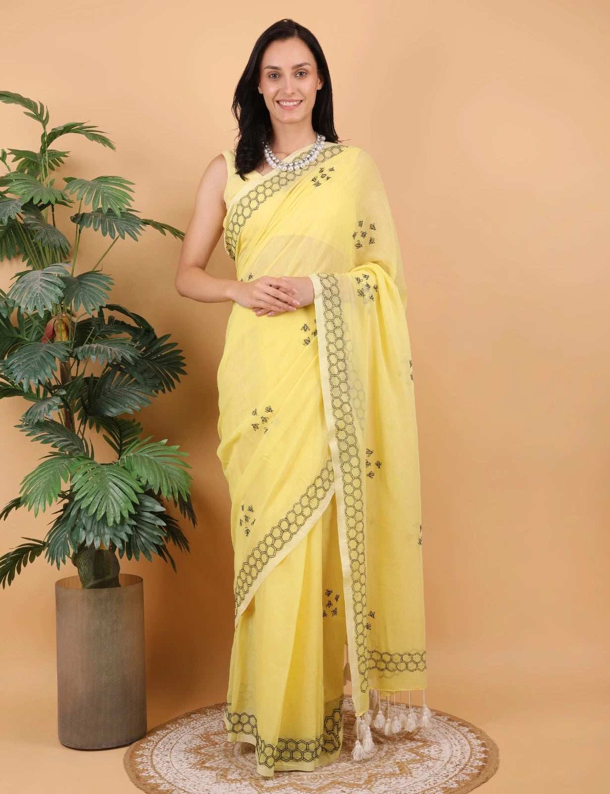 Woman wearing a yellow Mulmul saree with a plant and beige wall in the background