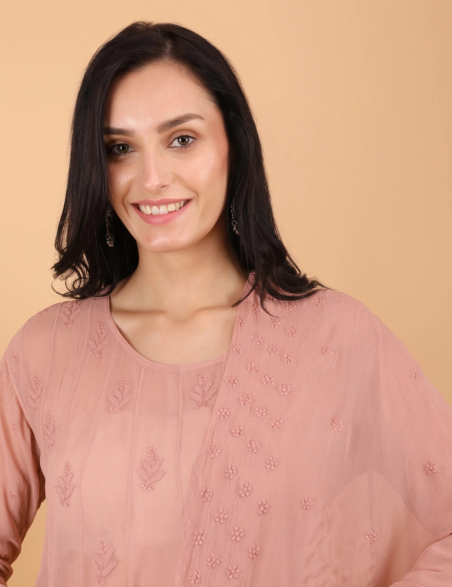 Woman wearing a pink embroidered top against a beige background