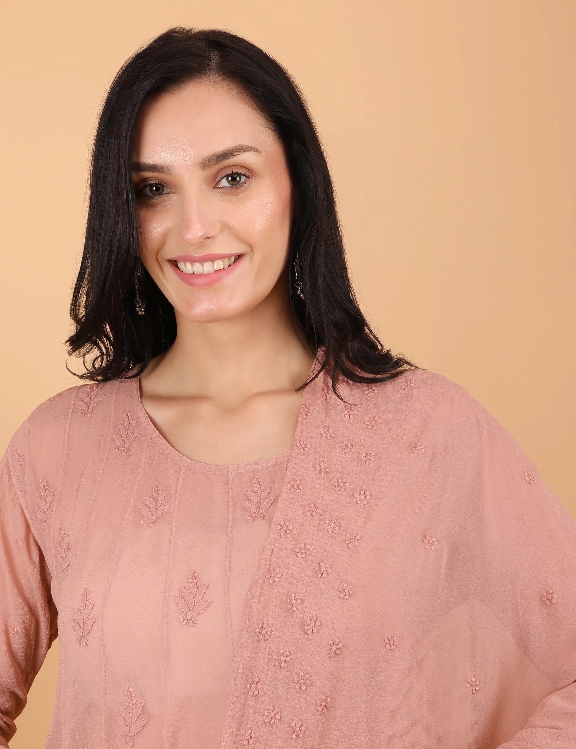 Woman wearing a pink embroidered top against a beige background