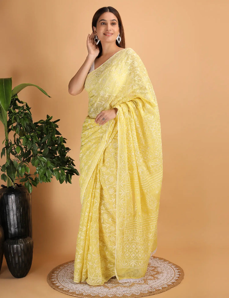 Woman in a yellow Hand Embroidered Chikankari saree standing next to a plant on a beige background