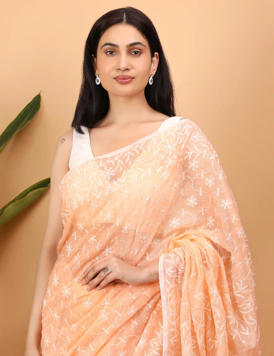 Woman wearing a peach  Hand Embroidered Chikankari saree with white patterns against a beige background
