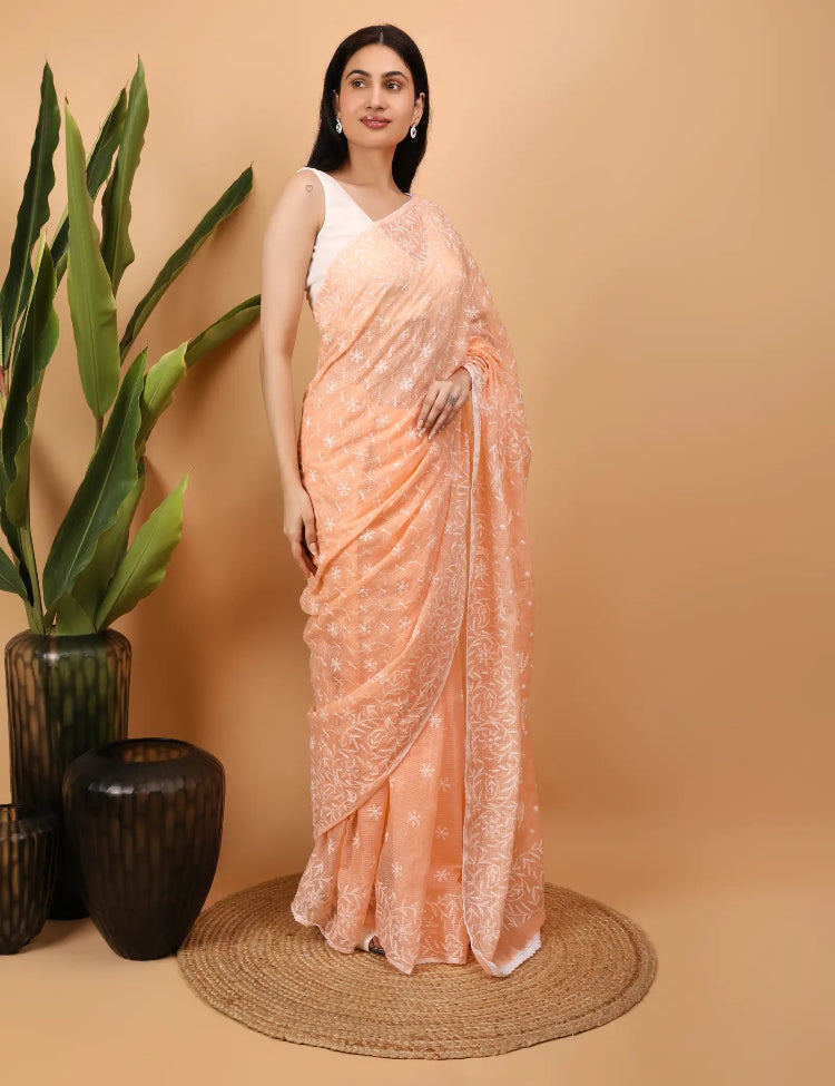 Woman wearing a peach Hand Embroidered Chikankari saree with a beige background