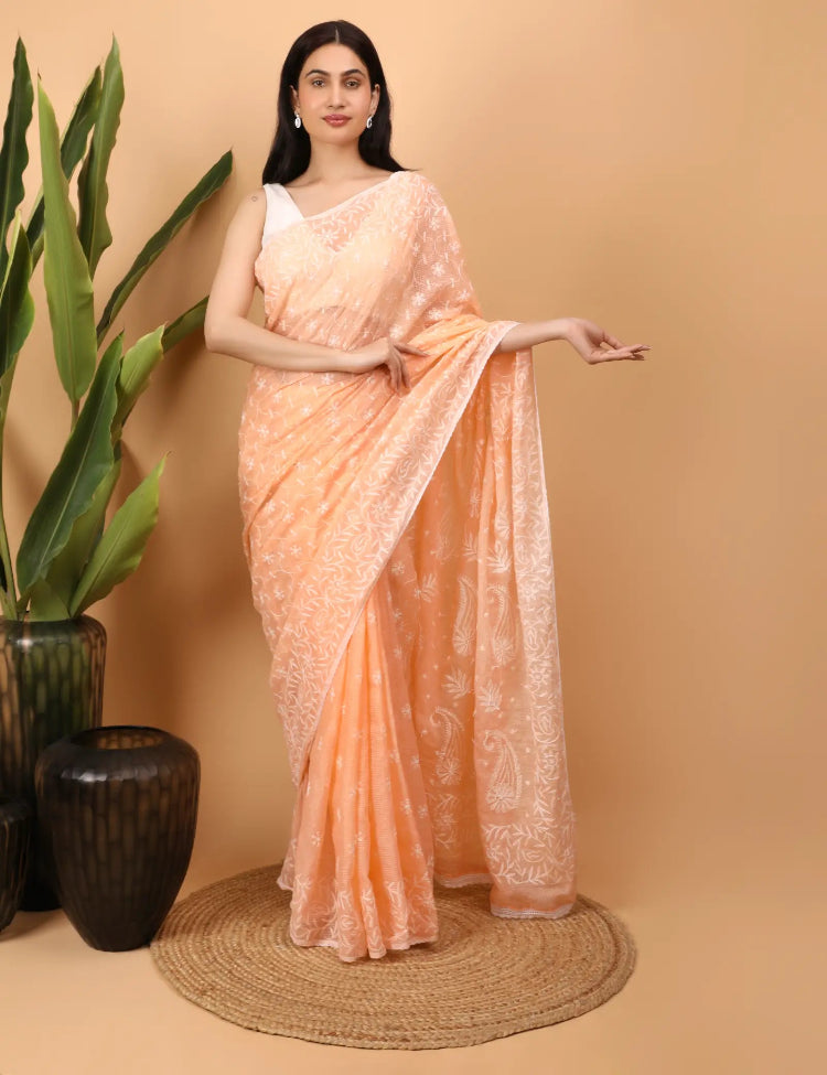 Woman wearing a peach Hand Embroidered Chikankari saree with a beige background