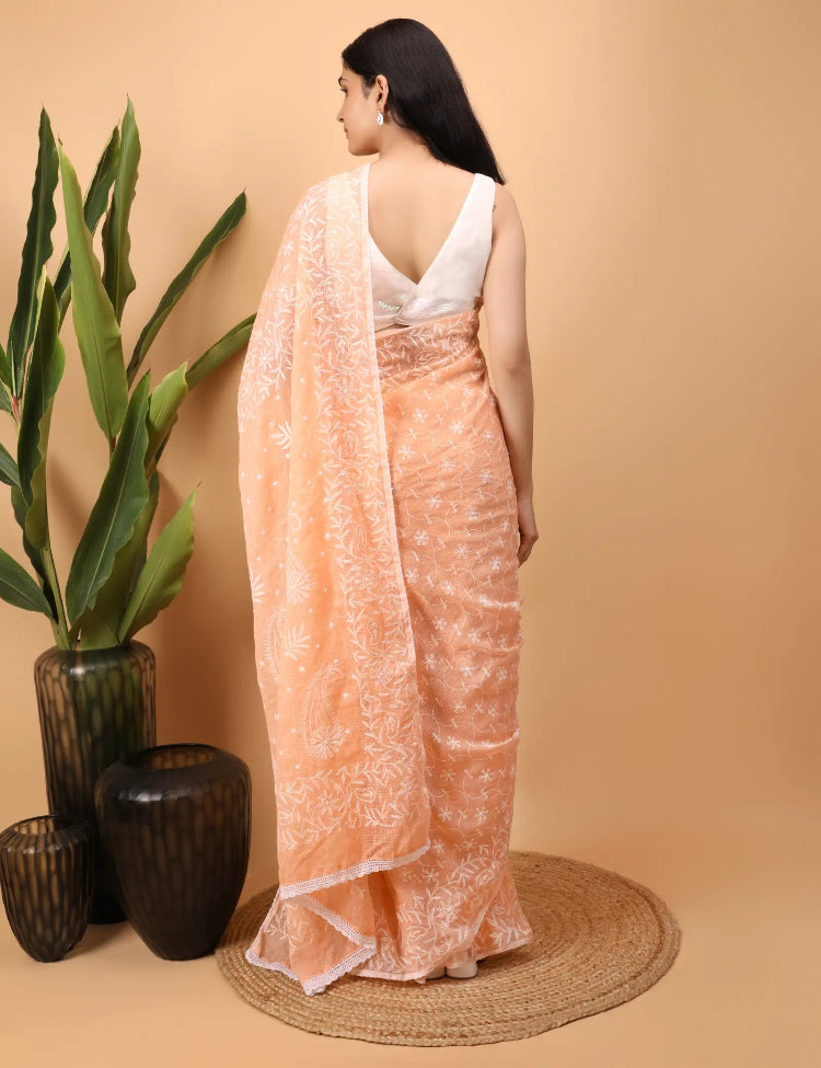 Woman wearing a peachHAnd Embroidered   Chikankari saree with a white blouse against a beige background