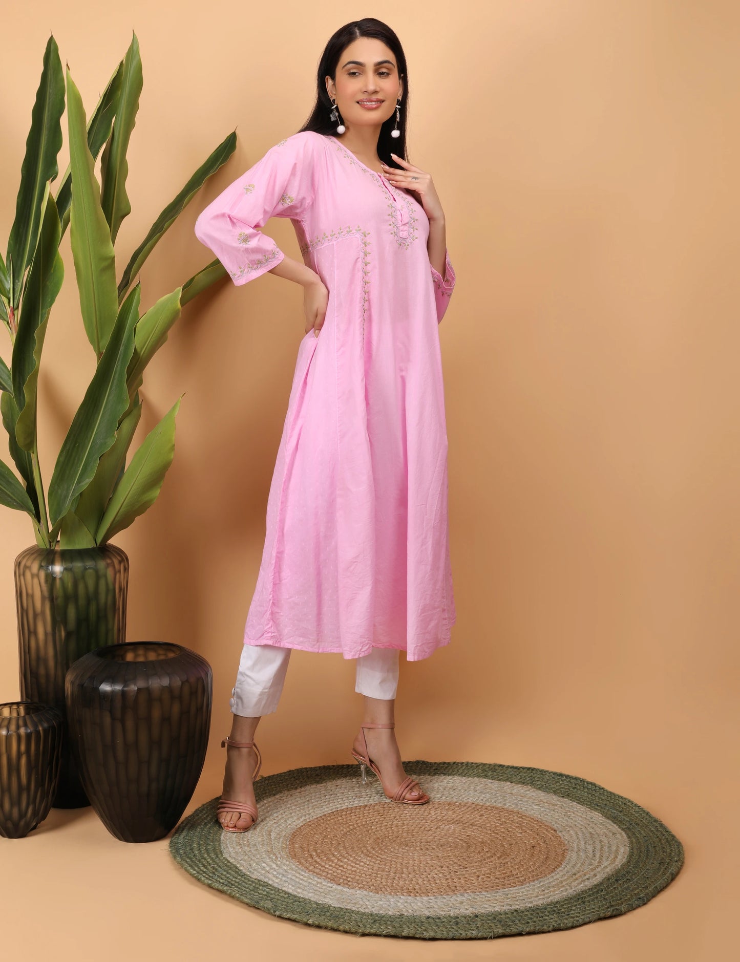 Woman in a pink kurta standing next to decorative vases on a beige background
