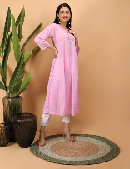 Woman in a pink kurta standing next to decorative vases on a beige background
