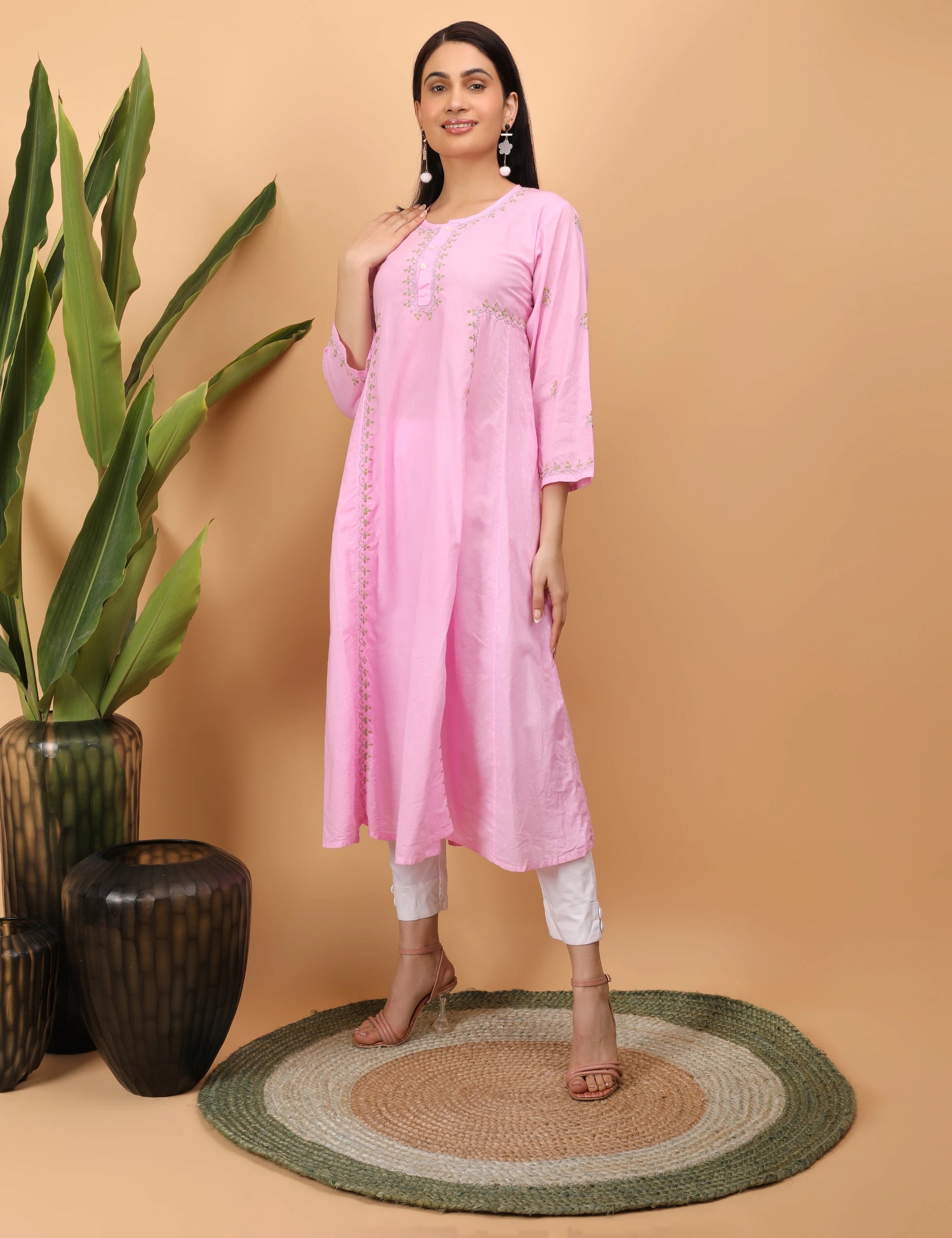 Woman wearing a pink kurta with white pants against a beige background