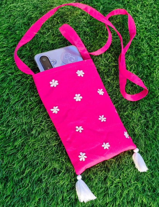 Pink pouch with white floral patterns and tassels on a grass background