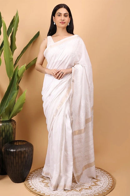 Woman in a white Hand Embroidered Chikankari saree standing next to a plant on a beige background