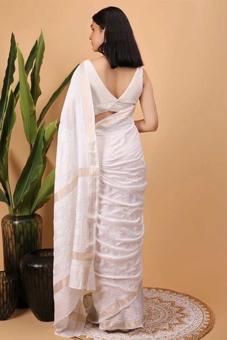 Woman in a  white Hand Embroidered Chikankari saree standing next to a plant on a beige background