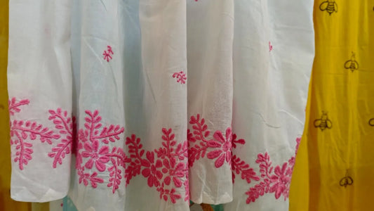 White fabric with pink Chikankari  embroidery next to a yellow garment with black patterns.