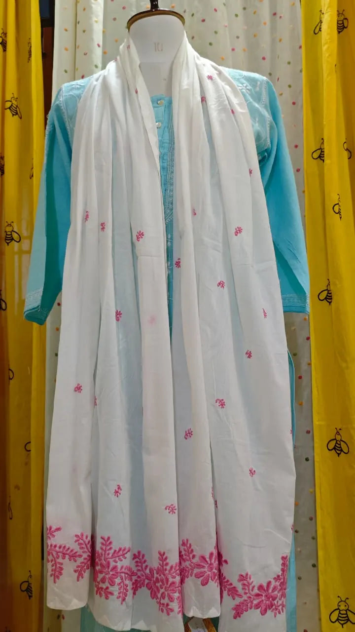 White scarf with pink floral patterns draped over a turquoise garment on a mannequin against a yellow curtain background.