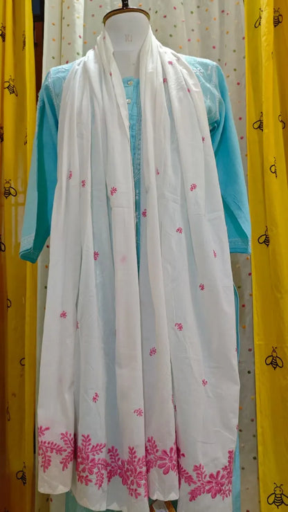 White scarf with pink floral patterns draped over a turquoise garment on a mannequin against a yellow curtain background.