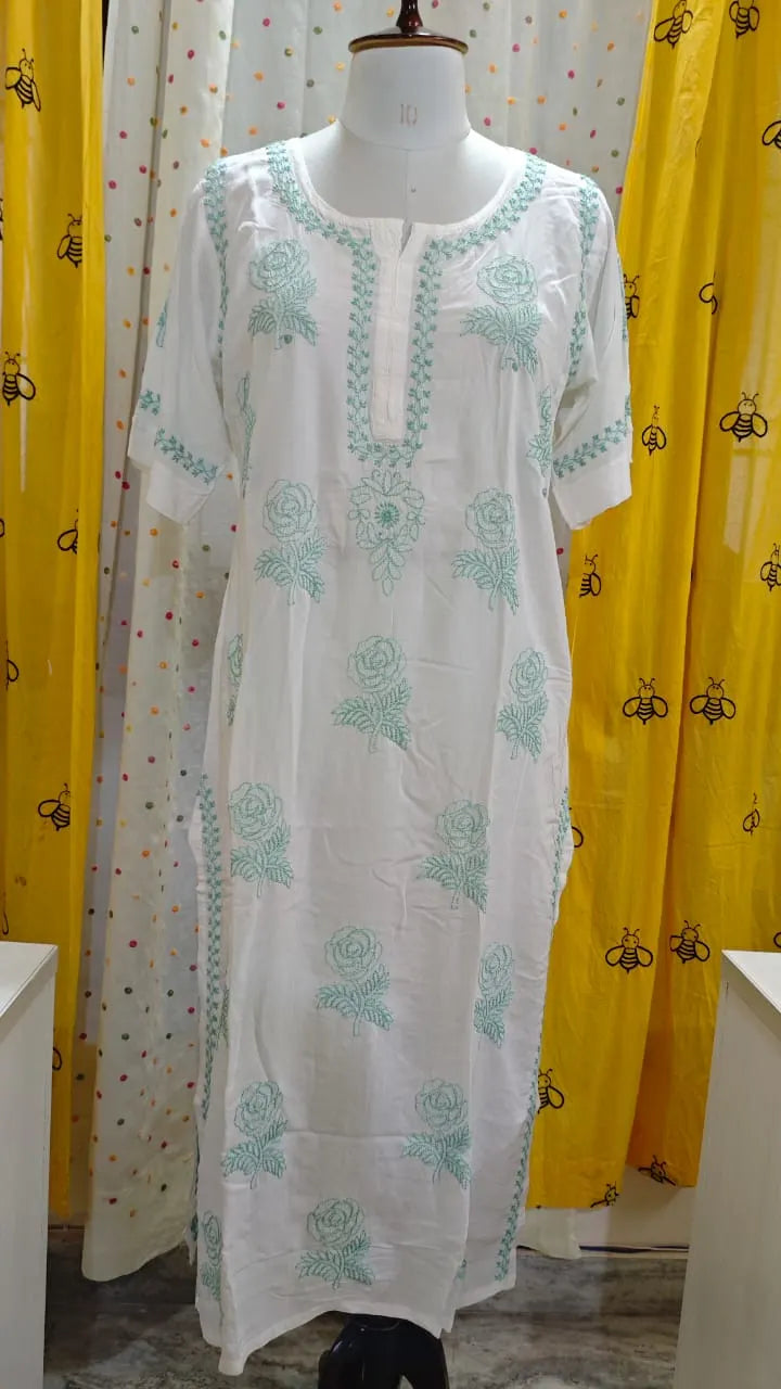 White kurta with green embroidery on a mannequin against a yellow curtain background