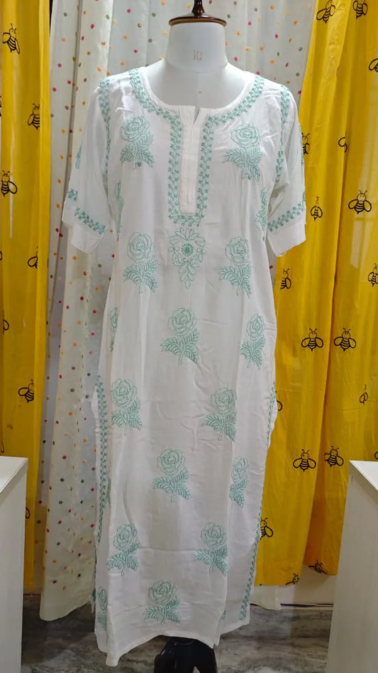White kurta with green embroidery on a mannequin against a yellow curtain background