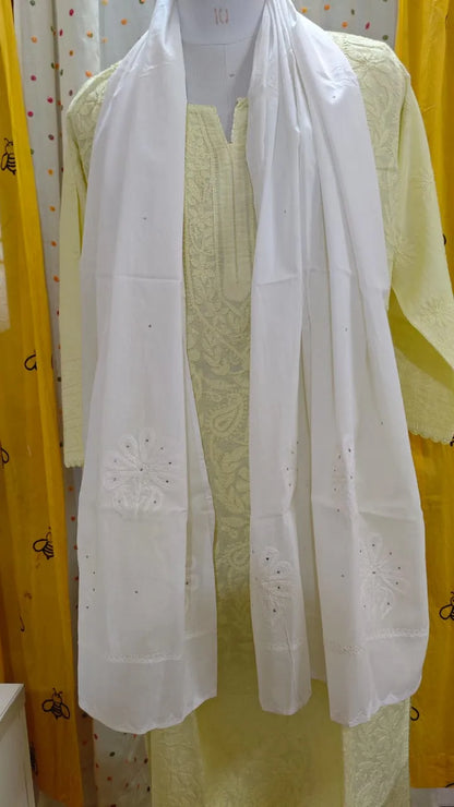 White embroidered scarf draped over a yellow garment with yellow curtains in the background