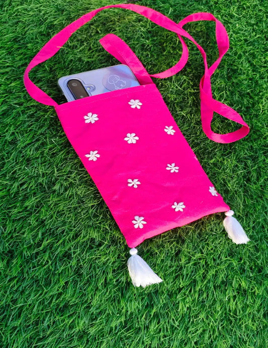 Pink pouch with white floral patterns and tassels on a grass background