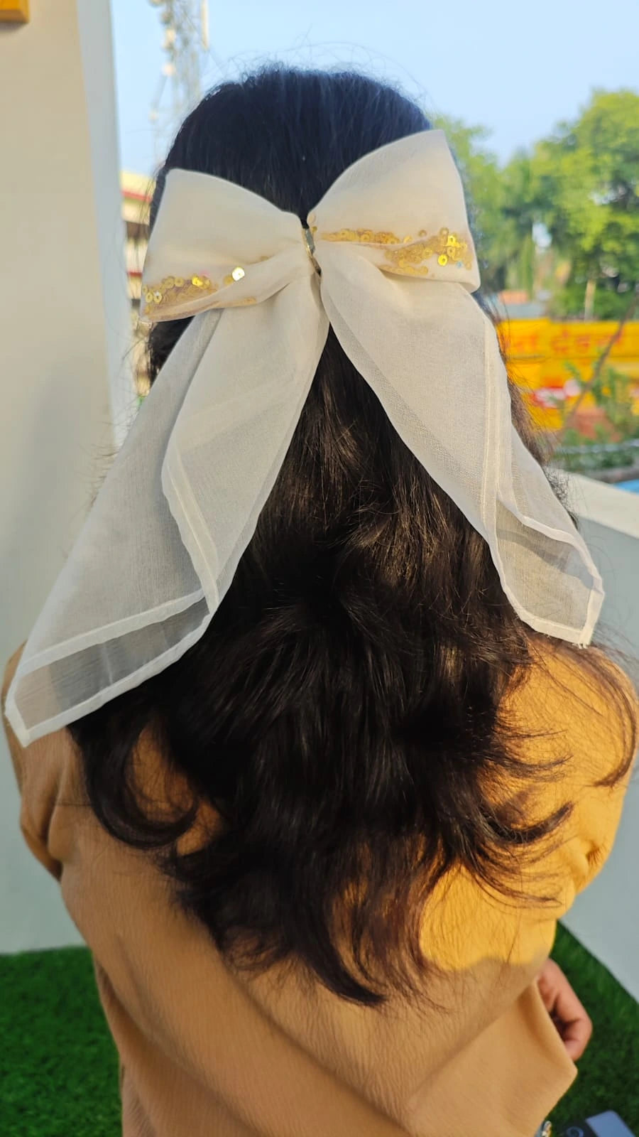 Person wearing a large white bow on their head with a blurred outdoor background