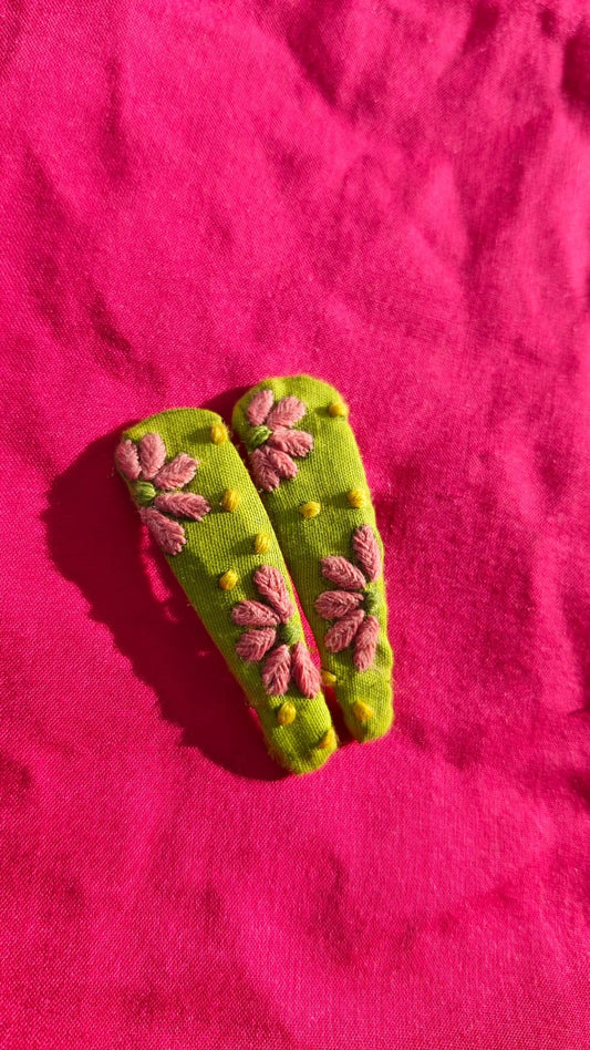 Green clips with pink floral hand embroidered chikankari decorations on a pink fabric background