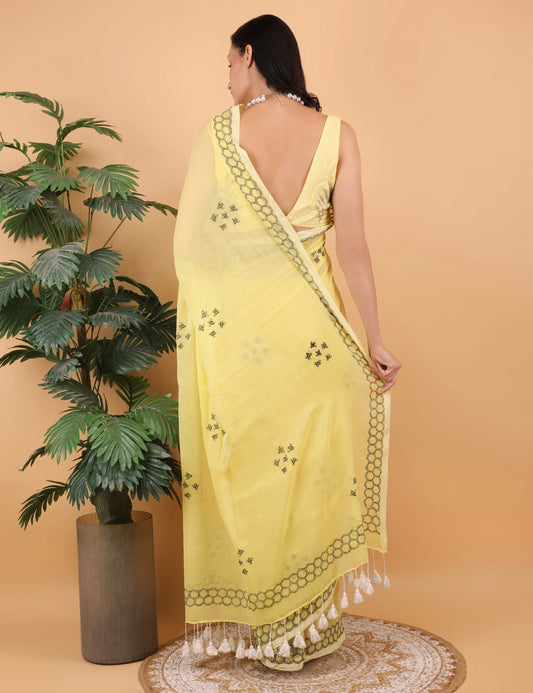 Woman wearing a yellow Mulmul saree with a plant and rug in the background